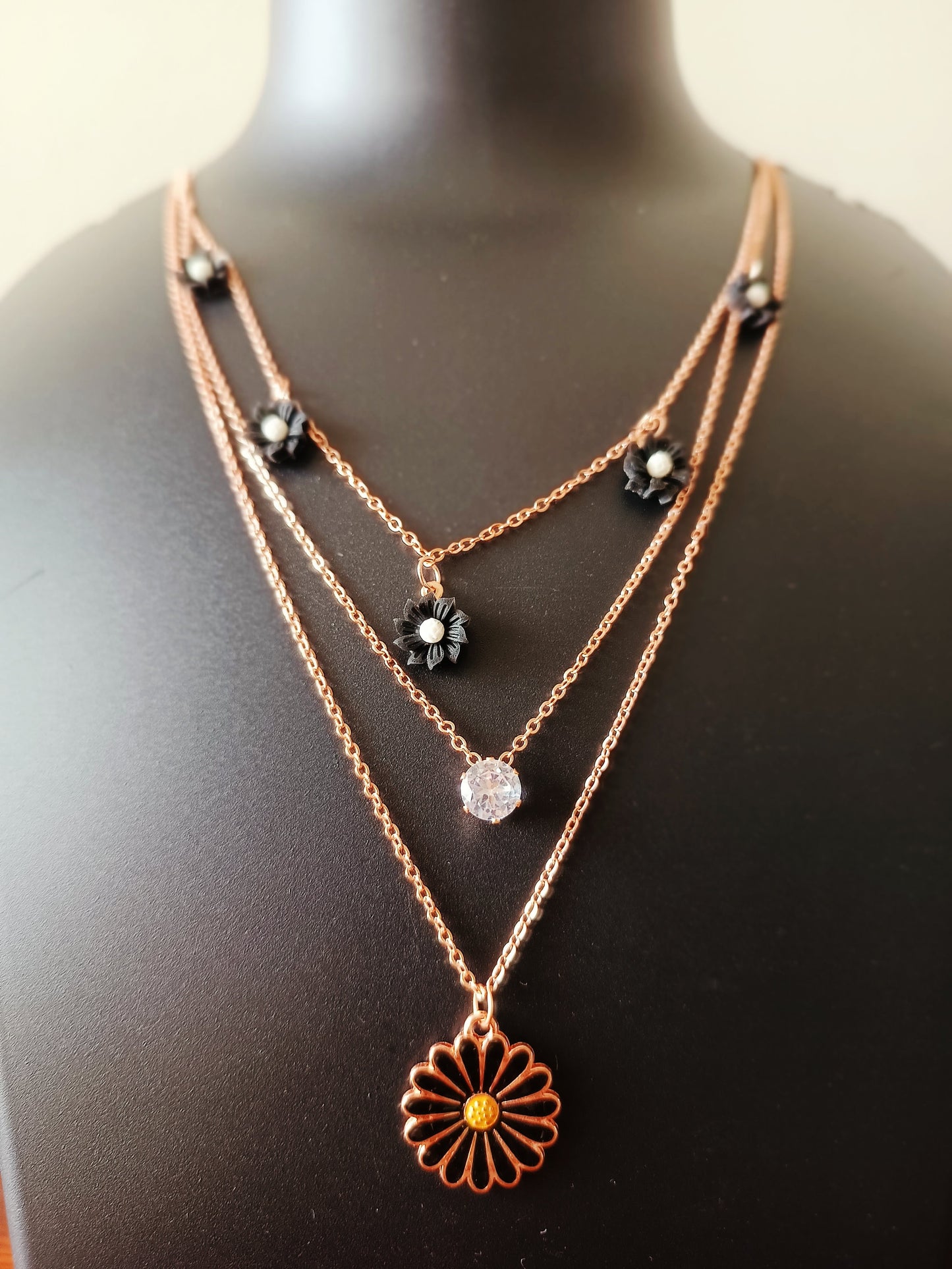 A rose-gold plated three-layered black daisy flowers neckpiece displayed on a mannequin bust.