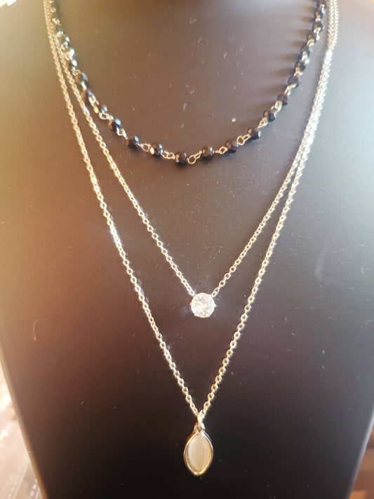 A silver-plated three-layered necklace with a raindrop-shaped pendant, displayed on a mannequin bust.