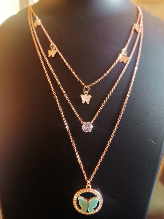 A rose-gold plated three-layered necklace with a teal-colored butterfly pendant, displayed on a mannequin.