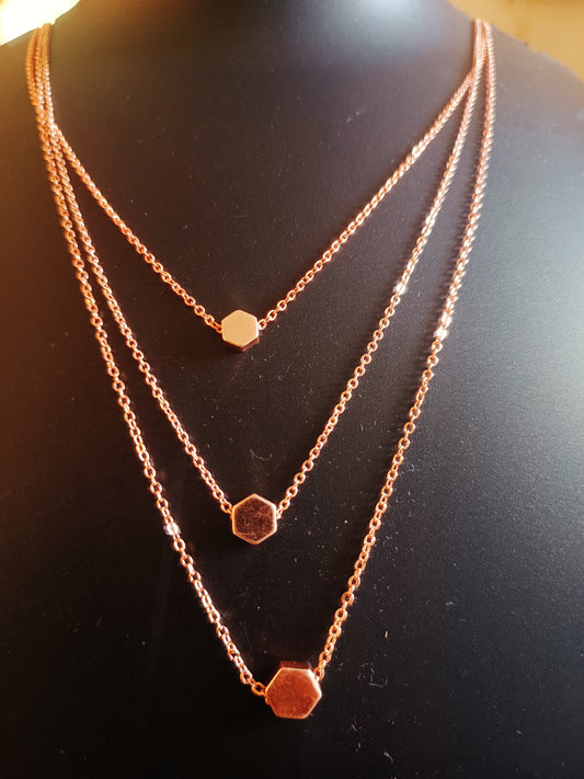 A rose-gold plated three-layered pentagon neckpiece displayed on a mannequin.