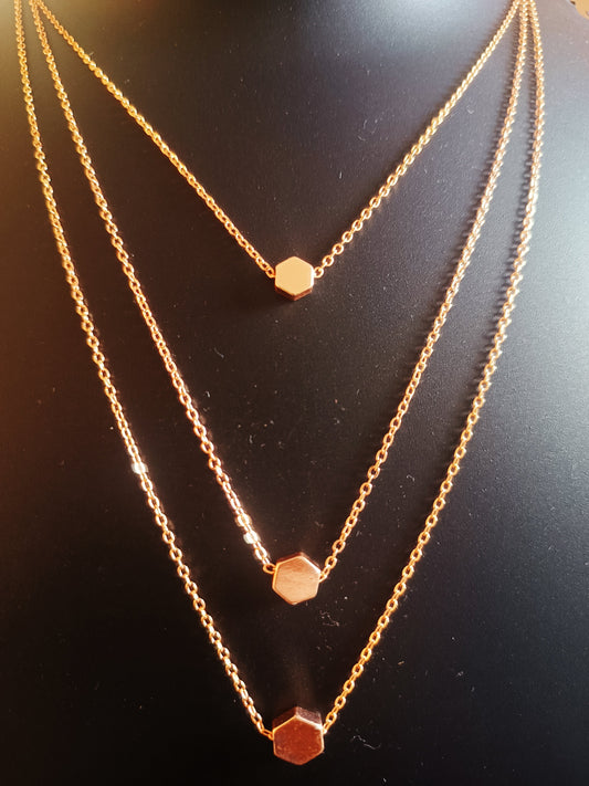 A gold-plated three-layered pentagon neckpiece laid out on a flat surface.