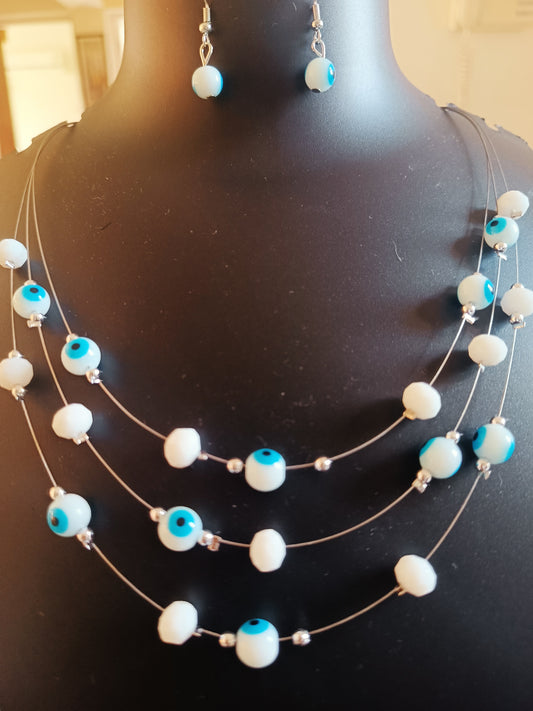 A three-layered necklace featuring white beads and blue evil eye beads, displayed on a mannequin bust.