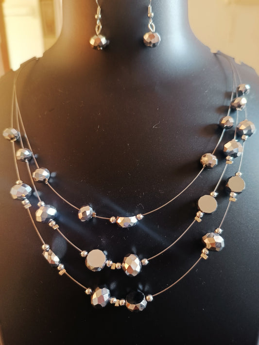 A three layered silver chromatic beads neckpiece with matching earrings displayed on a mannequin.