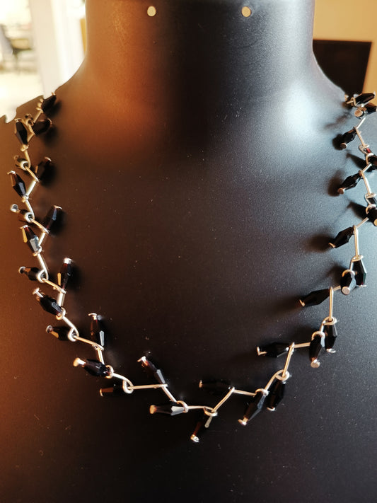 A silver-plated necklace with black disco beads displayed on a mannequin bust.