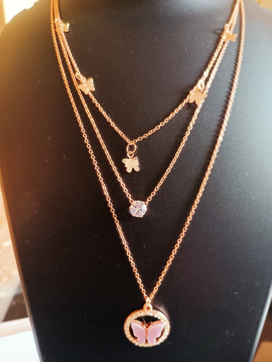 A rose-gold-plated three-layered butterfly neckpiece with pink color details on the butterflies and a circular pink pendant on the bottom layer.