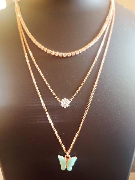 A rose-gold plated, diamond-studded, three-layered necklace with teal-colored butterfly charms on a mannequin bust.
