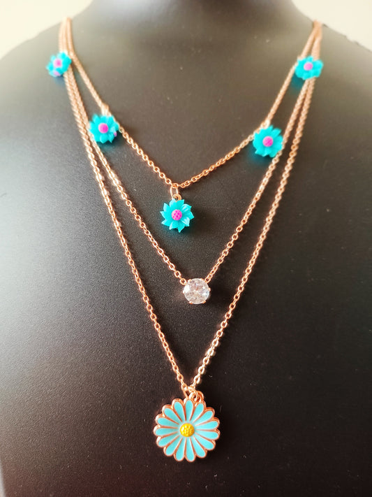 A rose-gold plated three-layered necklace with sky-blue daisy flowers pendants displayed on a mannequin.